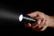 Male hand holding a led flashlight with a wide white beam on a black background, leaving the right side of the frame