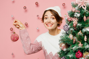 Wall Mural - Close up merry young woman wearing white sweater hat posing decorate Christmas tree with toys show bubble isolated on plain pastel pink background studio. Happy New Year celebration holiday concept.