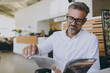 © ViDi Studio - Male happy calm rich smiling confident businessman man wears classic shirt read catalog sitting at office table in dealership store indoors want to buy new automobile car. Business lifestyle concept.