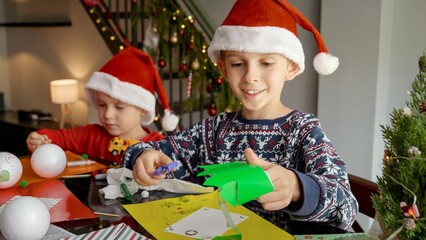 Two little boy preparing for Christmas cutting out paper decorations and garlands. Winter holidays, family time together, kids with parents celebrating.