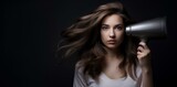 A beautiful girl dries her hair with a hair dryer, on a dark background.
