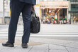 A businessman in suit uniform with briefcase bag is waiting to crossing the road in the city during working rush hour. Office working people routine lifestyle scene.