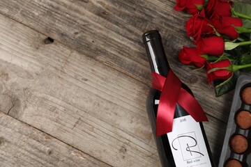 Wall Mural - Bottle of red wine, chocolate truffles and roses on wooden table, flat lay. Space for text