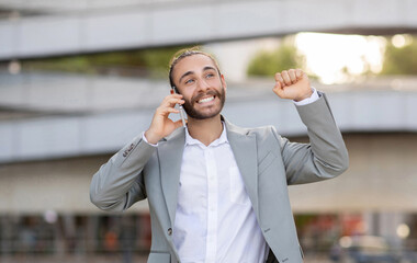 Joyful young businessman celebrating success during outdoor phone call