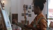 © Natee Meepian - Young African American stylish female pretty artist painting impressionism picture on canvas and creating artwork in art studio
