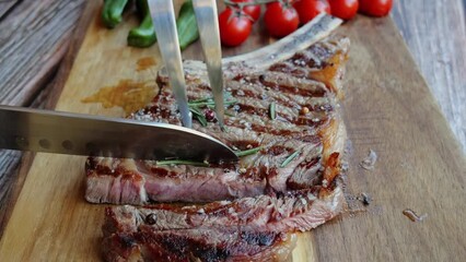 Sticker - T bone beef steak on board cut with a knife. Close up. Slow motion