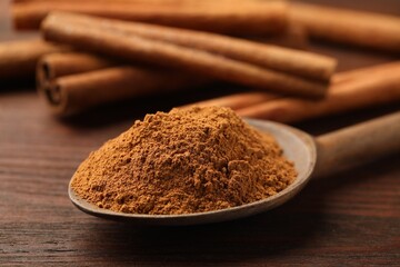 Wall Mural - spoon with cinnamon powder and sticks on wooden table, closeup