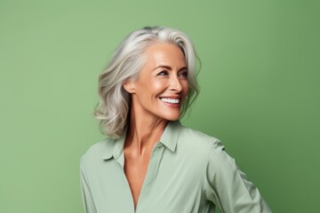 Cheerful mature woman looking at camera and smiling while standing against green background