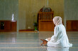 © maya1313 - The image of an Asian Muslim woman in the Islamic religion in hijab in cream color. reading the Quran and having a happy Staying in a beautiful mosque, Arabic word translation: The Holy Al Quran.
