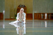 © maya1313 - The image of an Asian Muslim woman in the Islamic religion in hijab in cream color. reading the Quran and having a happy Staying in a beautiful mosque, Arabic word translation: The Holy Al Quran.