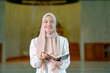 © maya1313 - The image of an Asian Muslim woman in the Islamic religion in hijab in cream color. reading the Quran and having a happy Staying in a beautiful mosque, Arabic word translation: The Holy Al Quran.