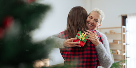 Wall Mural - Thankful Caucasian woman with christmas gift hugging daughter at home