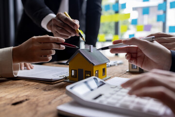 Real estate agents offer contracts to buy or rent housing. Businessman holding model small building house with property insurance at table in home sales office
