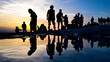 Silhouettes of people are reflected in the water and the crowded group watches the sunset.