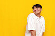 modest young asian guy in white t-shirt is shy and smiling on yellow isolated background, embarrassed korean man
