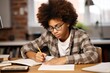 An African American teenager boy in eyeglasses does her homework at the table at home. He writes down solutions of tasks in her notebook.