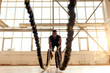 Wall Mural - african american athletic man in sportswear training in the gym and waving the ropes, athlete doing sports and fitness