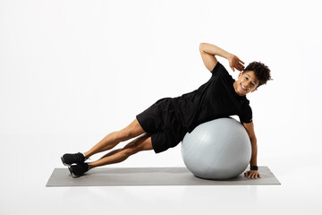 Wall Mural - man performs side plank exercise on balance ball, white background