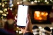 Unrecognizable Man Hands Using smartphone by fireplace at home, white blank empty screen display. Winter fun, lifestyle, leisure, holidays, vacations, Christmas, New Year, web site, technology