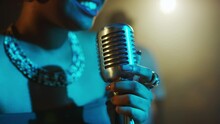 Medium Closeup Of Attractive Young Black Woman Singing Blues In Retro Microphone While Performing Life On Stage With Blue Light Of Projector On Her Face