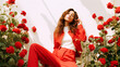 © Tamara - A beautiful girl with brown hair in a white T-shirt and a red suit sits among red roses in a white studio
