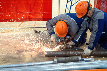 Poster - Two workers are sawing pipe. Craftsmen produce steel pipeline. Process of installing pipes inside building. Construction of engineering communications. Factory craftsmen sawing off piece of pipe