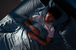 © mtrlin - Top View of Arabic young man sleeping on a bed in his bedroom at night. Blue nightly light shining through the window.