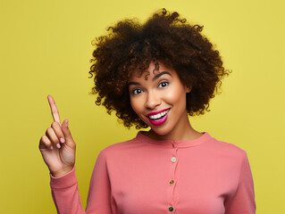 Portrait of cute curly African American woman pointing with finger yellow background