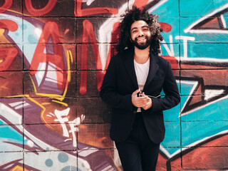 Handsome hipster model. Arabian man dressed in suit jacket clothes. Fashion male with long curly hairstyle posing in street near graffiti wall