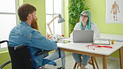 Canvas Print - Man and woman doctor and patient having medical consultation siting on wheelchair at clinic