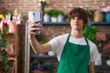 Young blond man florist make selfie by smartphone at flower shop