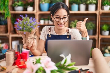 Canvas Print - Young hispanic woman working at florist shop doing video call doing happy thumbs up gesture with hand. approving expression looking at the camera showing success.