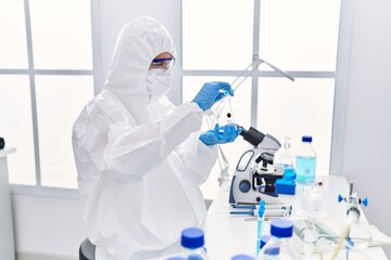 Poster - Young blonde woman scientist wearing security uniform pouring liquid on test tube at laboratory