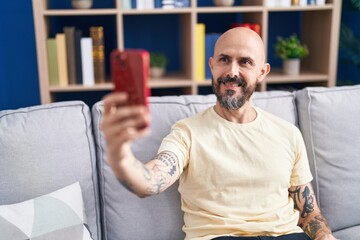 Wall Mural - Young bald man make selfie by smartphone sitting on sofa at home