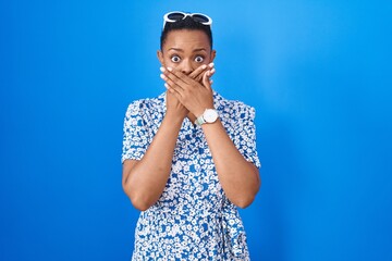 Sticker - African american woman standing over blue background shocked covering mouth with hands for mistake. secret concept.