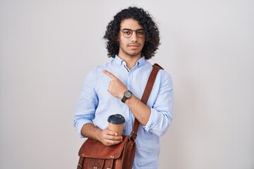 Poster - Hispanic man with curly hair drinking a cup of take away coffee pointing with hand finger to the side showing advertisement, serious and calm face