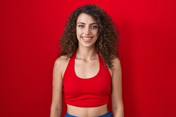 Sticker - Hispanic woman with curly hair standing over red background with a happy and cool smile on face. lucky person.