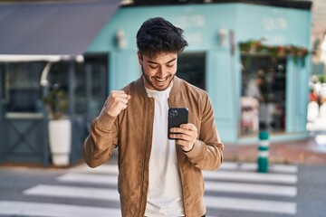 Canvas Print - Young hispanic man smiling confident using smartphone at street