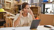 © Krakenimages.com - Spotlight on a young, beautiful hispanic woman carpenter, in-depth conversation over smartphone at her carpentry workshop, balancing business and craftsmanship with touchpad