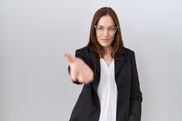 Poster - Beautiful brunette woman wearing business jacket and glasses smiling cheerful offering palm hand giving assistance and acceptance.