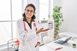 Young latin woman wearing doctor uniform doing coming gesture at clinic