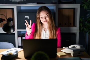 Canvas Print - Young caucasian woman working at the office at night showing and pointing up with fingers number three while smiling confident and happy.