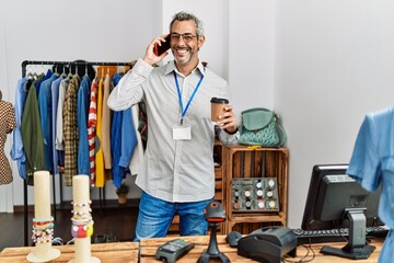 Wall Mural - Middle age grey-haired man shop assistant talking on smartphone drinking coffee at clothing store