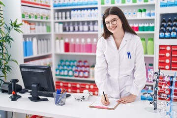 Wall Mural - Young caucasian woman pharmacist smiling confident writing on document at pharmacy