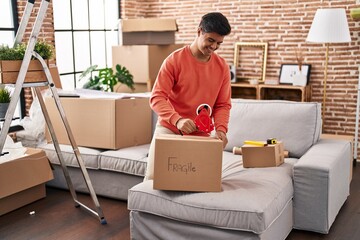 Wall Mural - Young hispanic man smiling confident packing cardboard box at new home