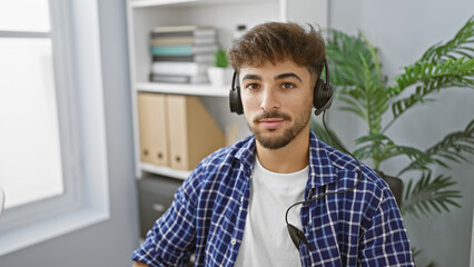 Poster - Handsome young arab man, a successful worker, concentrating on his job, wearing a headset indoors at the office. a professional with a relaxed demeanour, providing aid and service for customers.