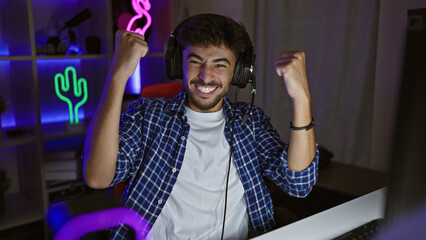 Canvas Print - Handsome young arab man, a confident gamer, streams night win at his video game, cheering in the gaming room, victorious smile lit by the screen glow.