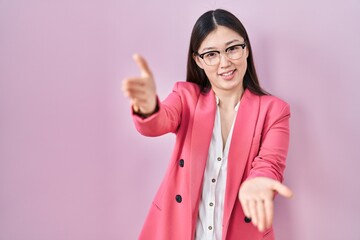 Wall Mural - Chinese business young woman wearing glasses looking at the camera smiling with open arms for hug. cheerful expression embracing happiness.