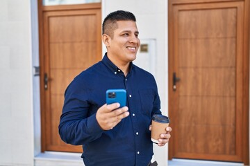 Wall Mural - Young latin man using smartphone drinking coffee at street