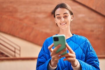 Wall Mural - Young caucasian woman smiling confident using smartphone at street